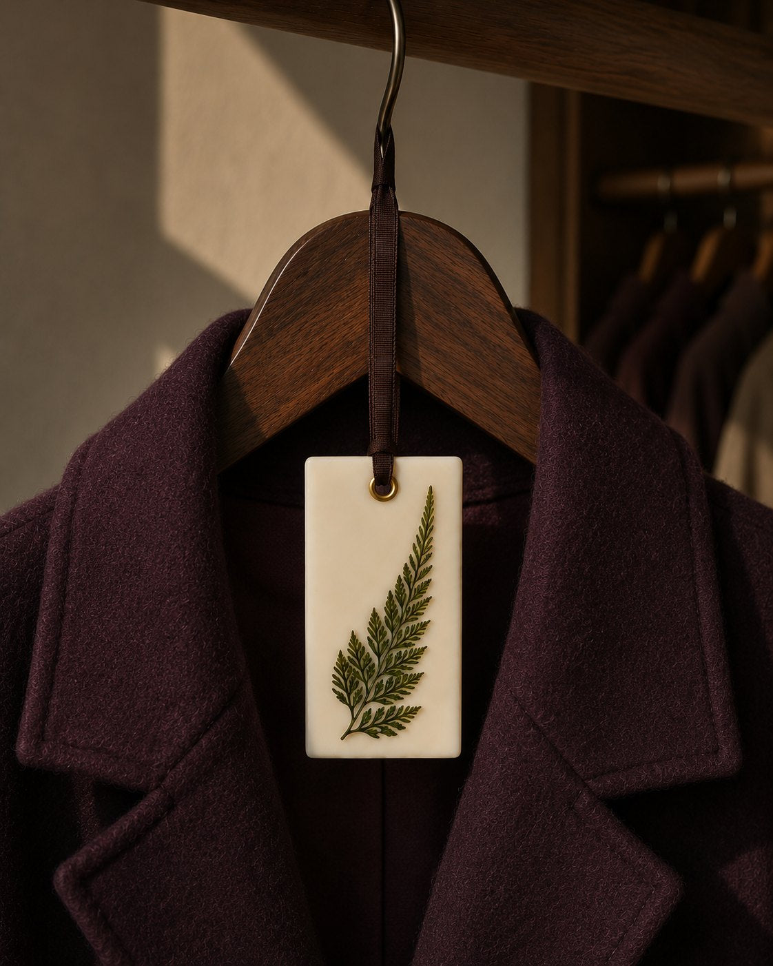 Ambientador de cera Sol&Vent con hoja de helecho colgado sobre una chaqueta granate