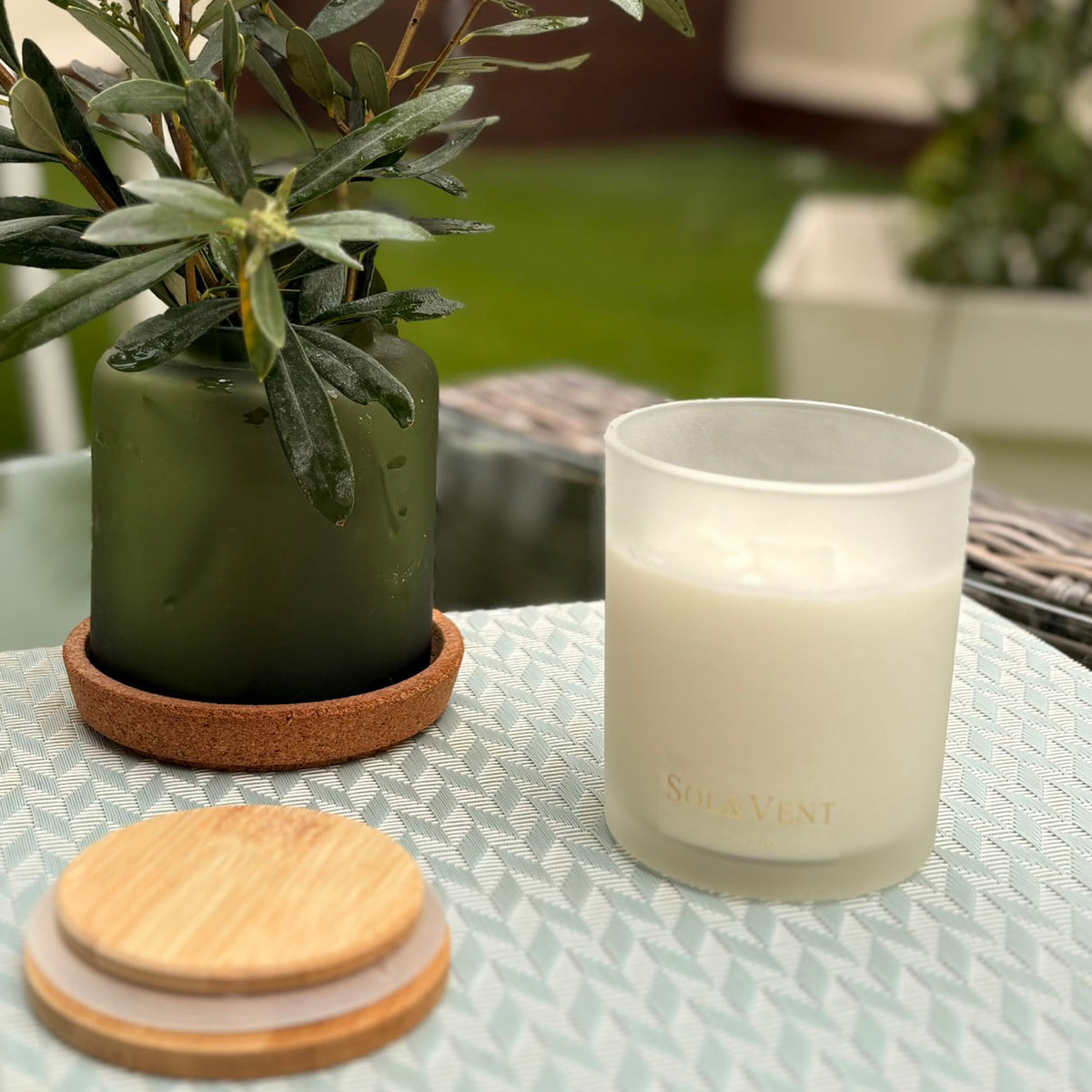 Vela perfumada Patio Andaluz de Sol&Vent junto a un olivo en maceta, sobre una mesa de exterior