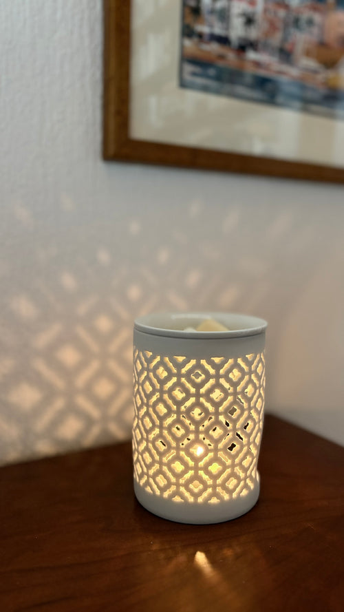 Quemador de cera Celosía encendido con una vela de té, proyectando sombras de su diseño calado en la pared