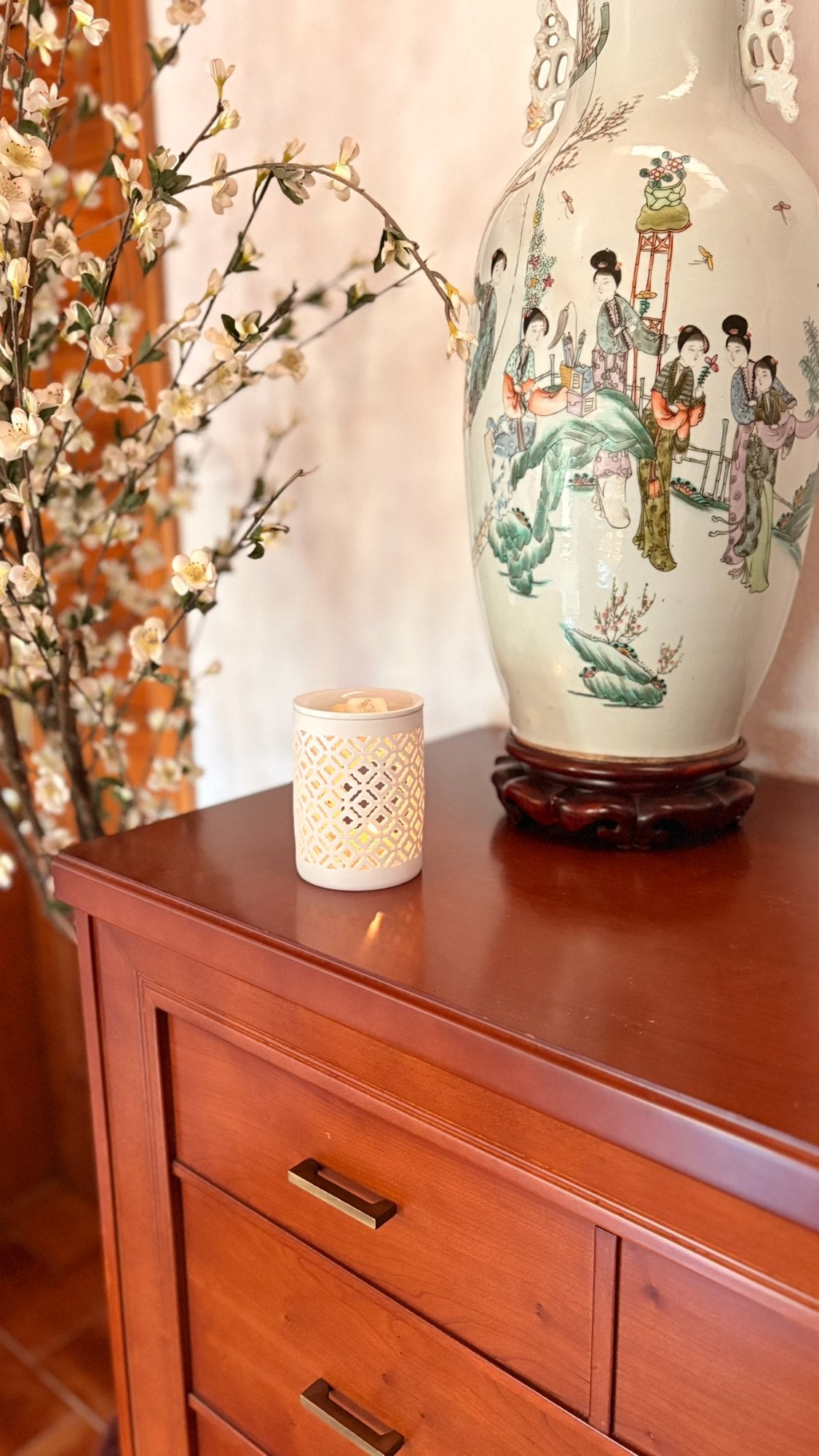Quemador de cerámica sobre una cómoda de madera junto a un jarrón de porcelana y ramas en flor
