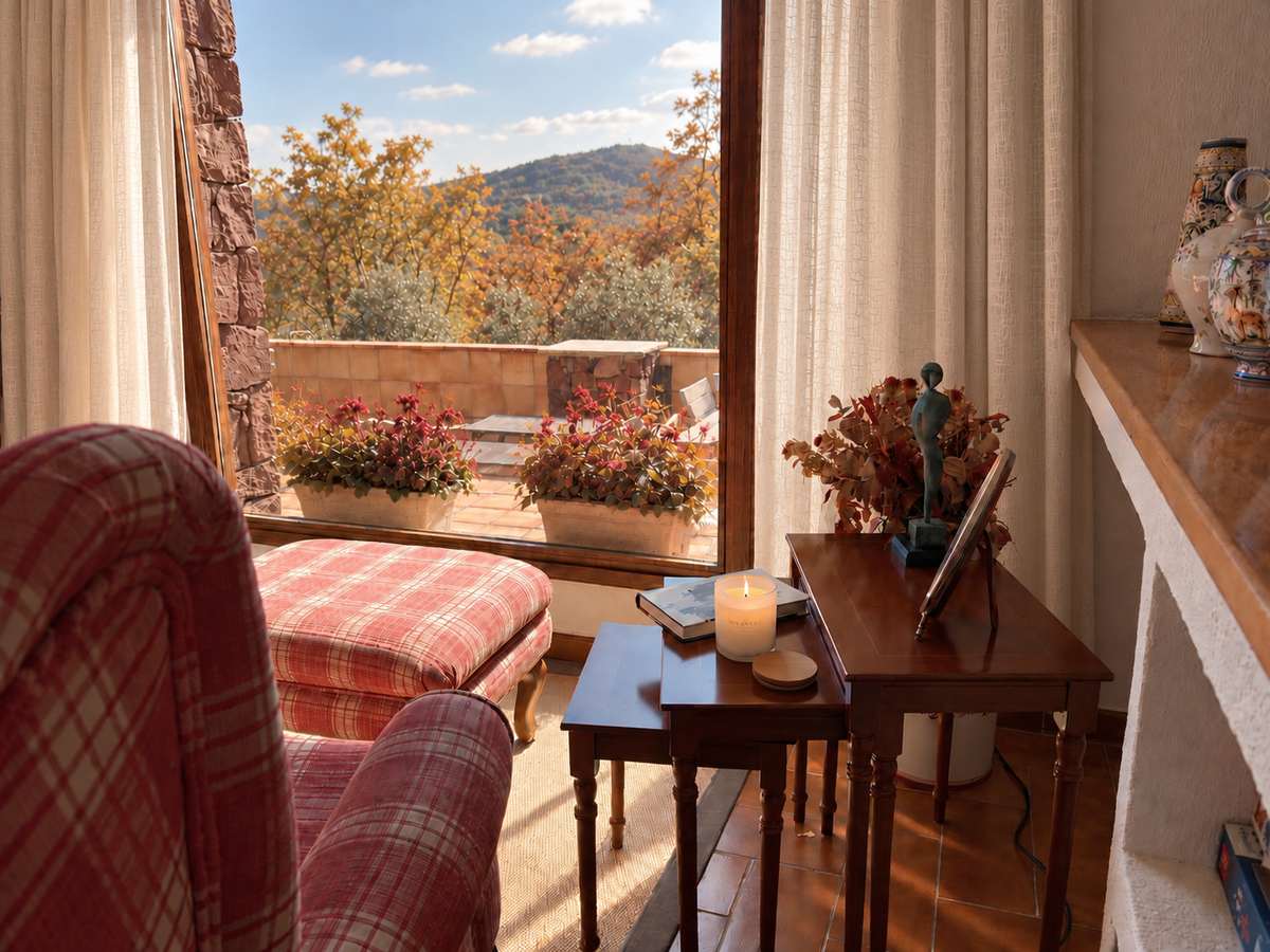 Vela perfumada Sol&Vent encendida junto a una terraza con vistas a la montaña en otoño, con butaca de cuadros y mesa de madera