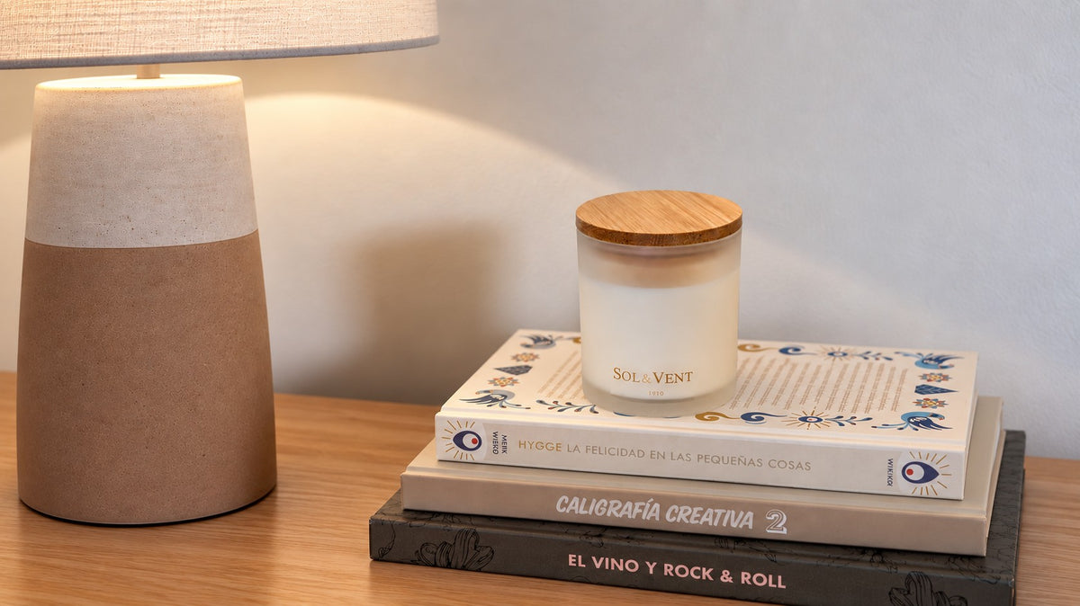 Vela perfumada Sol&Vent sobre una pila de libros junto a una lámpara de cerámica encendida