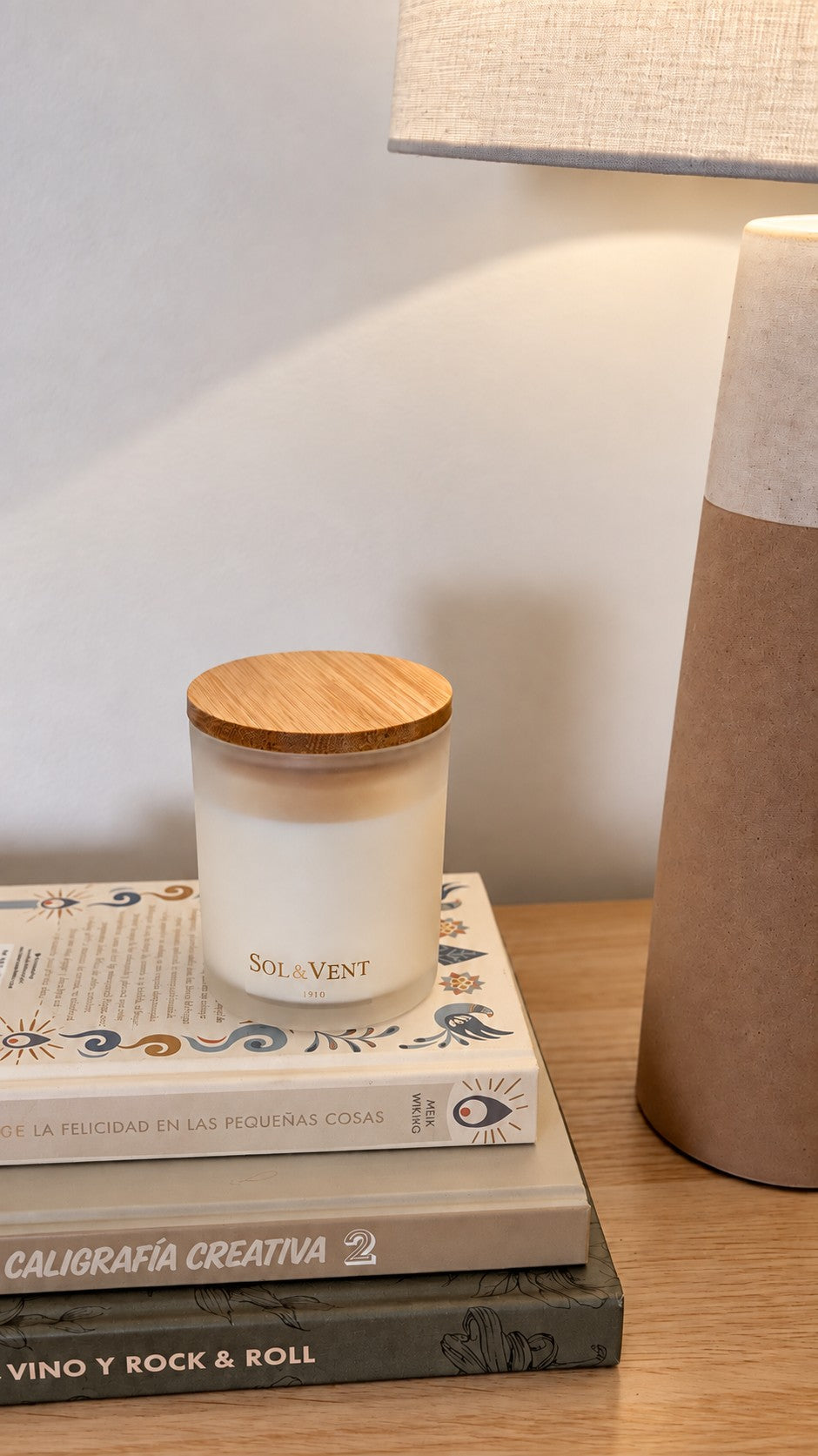 Vela perfumada Sol&Vent sobre una pila de libros junto a una lámpara de cerámica